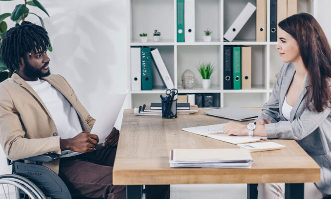homem negro em cadeira de rodas realizando entrevista de recrutamento pcd com profissional de rh em escritório