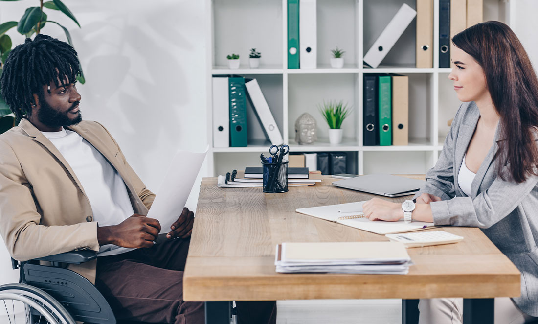 homem negro em cadeira de rodas realizando entrevista de recrutamento pcd com profissional de rh em escritório