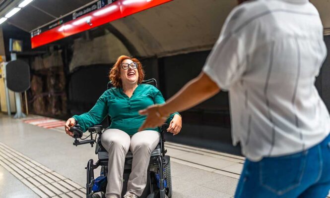 mulher em cadeira de rodas motorizada sorrindo em estacao de metro acessivel representando a importancia do ambiente no modelo biopsicossocial
