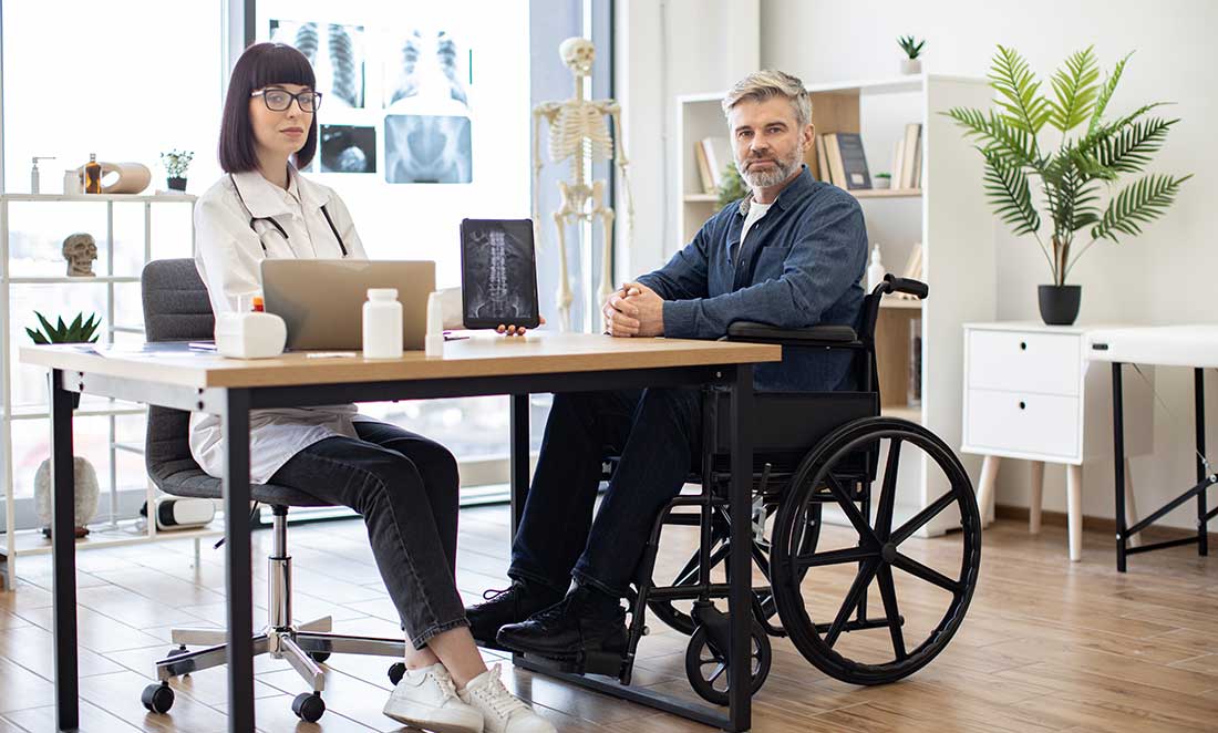 uma médica em seu escritório mostra um raio x em um tablet para um homem em uma cadeira de rodas este encontro ilustra o primeiro passo da avaliação biopsicossocial da deficiência